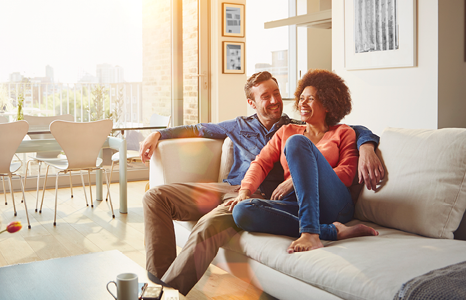 Couple Sitting on Couch in Living Room and Smiling on Sunny Day
