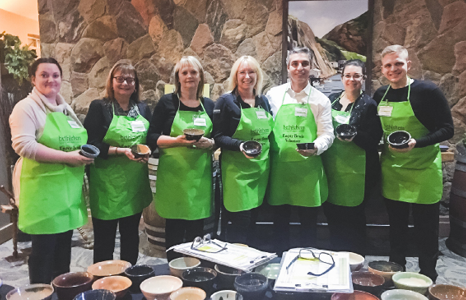 Seven People in Green Aprons Holding Bowls at Event