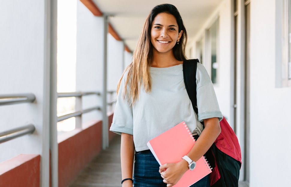 Student Standing in Hallway Smiling While Holding Pink Notebook
