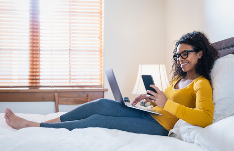 Woman Browsing Rates on Computer and Phone in Bed.png