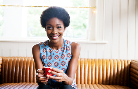 Woman Smiling While Holding an Espresso Cup and Sitting on Couch